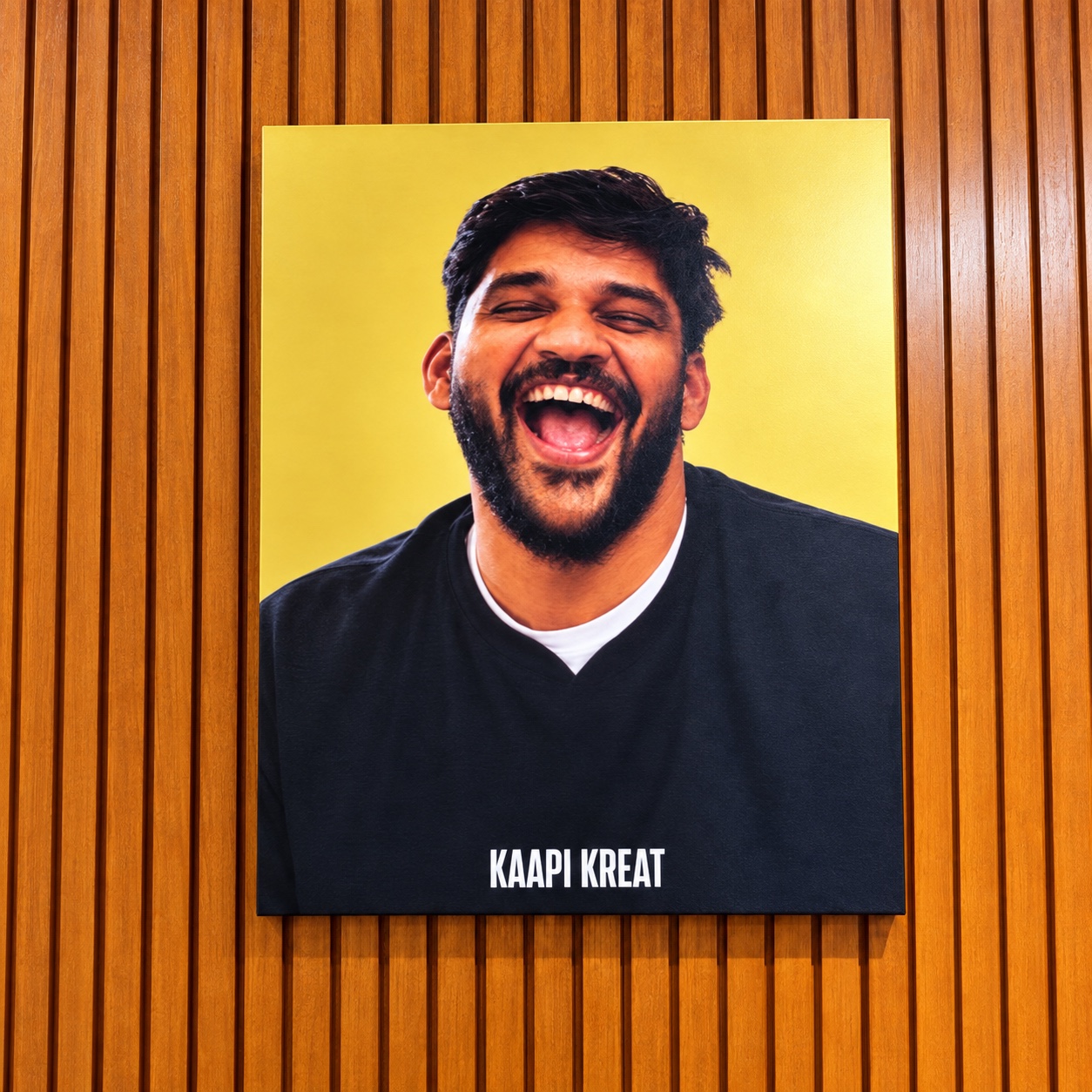 Joshua Michael laughing in a portrait mounted on Kaapi Kreat’s warm wooden wall